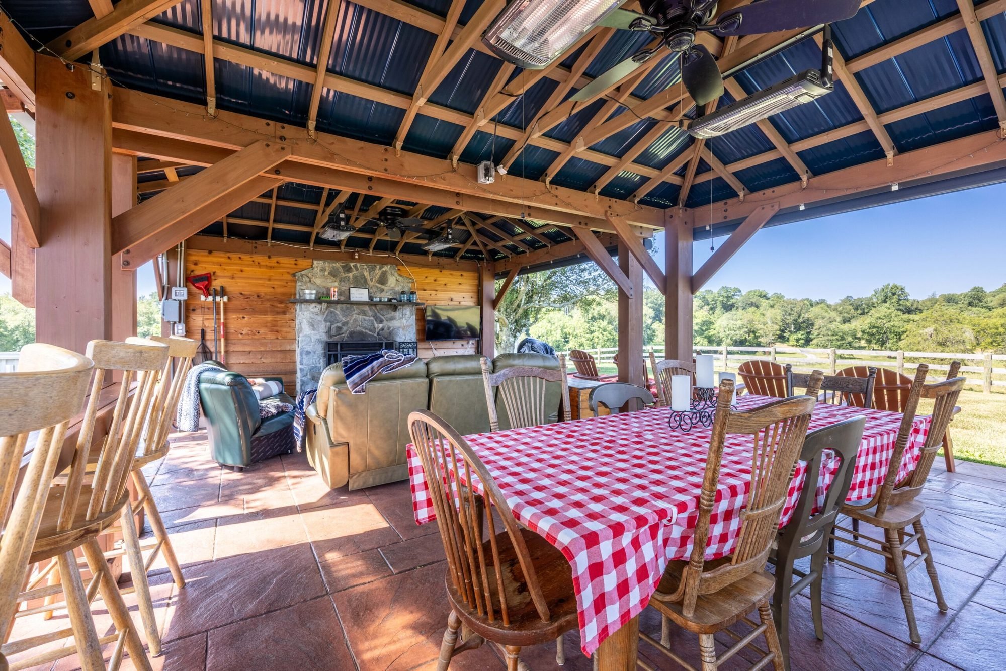 Covered pavilion with a long dining table, lounge seating and a stone fireplace